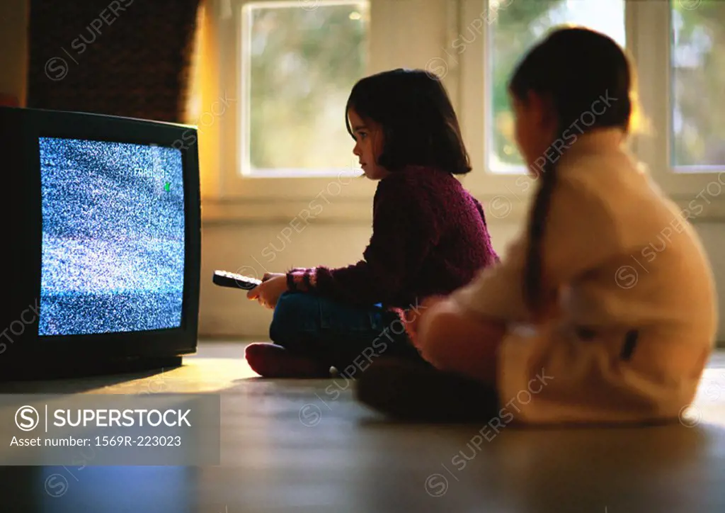 Young girls sitting on wood floor watching TV, girl in foreground blurred