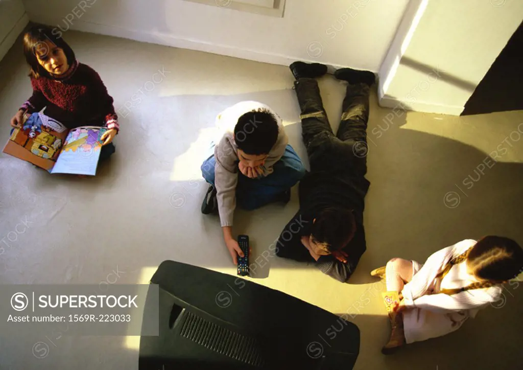 Young boys and girls sitting on floor watching TV, high angle view