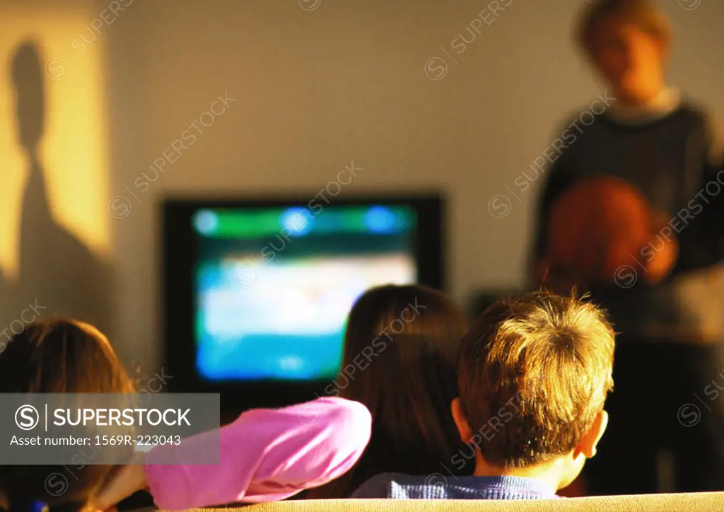 Young boys and girls watching TV, boy in distance blurred