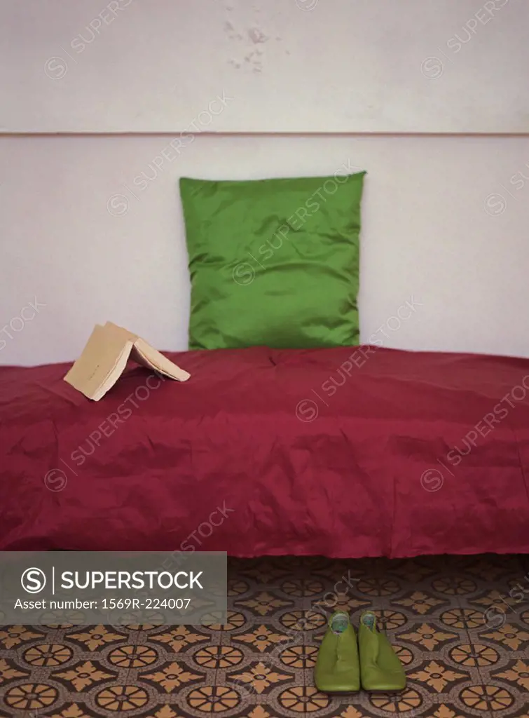Couch with open book and pillow on top, pair of shoes nearby