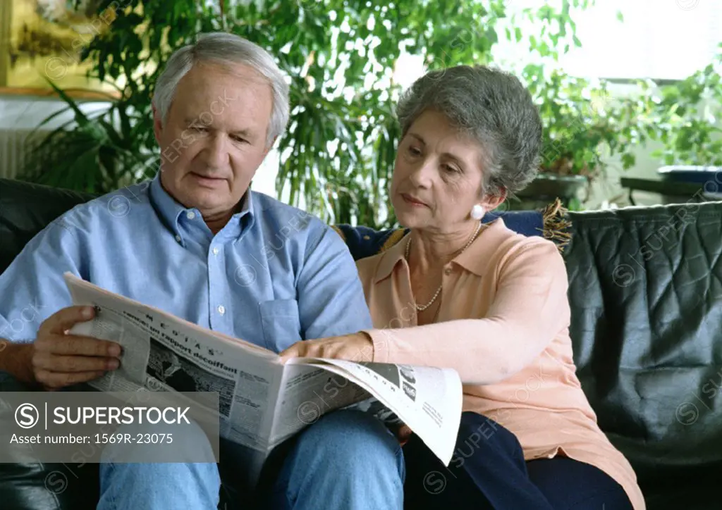 Senior couple on couch reading newspaper