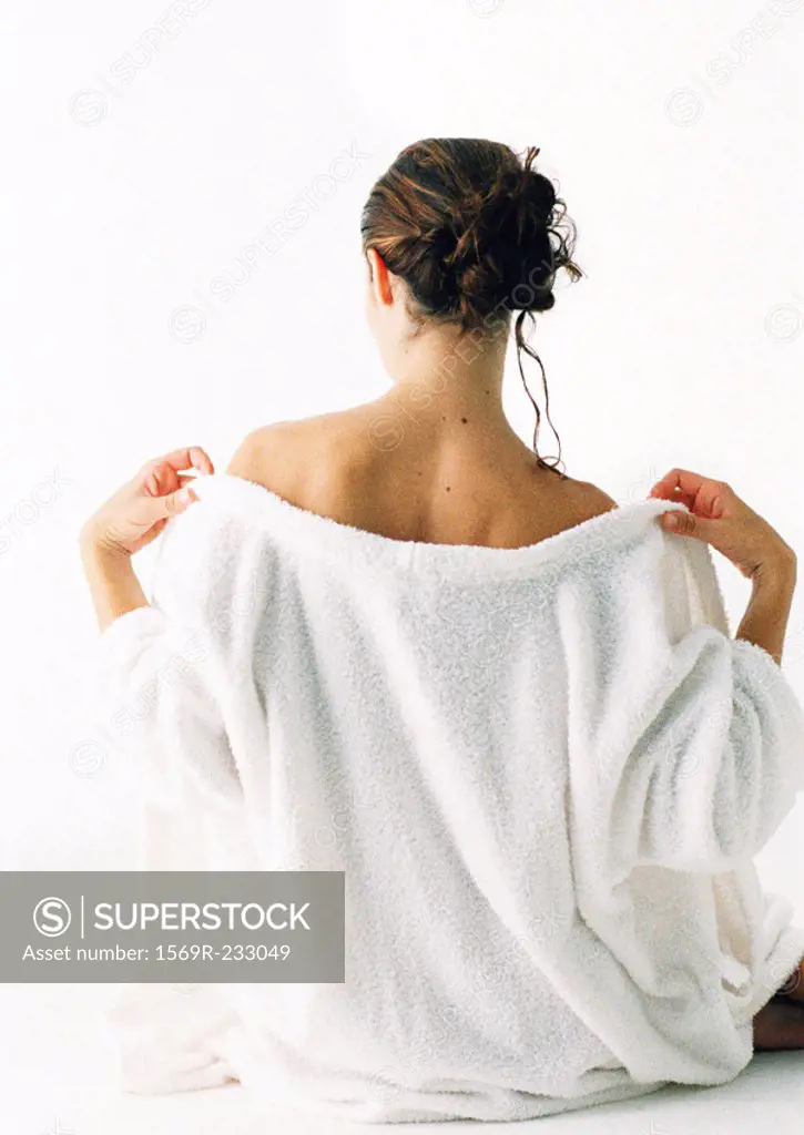 Woman sitting on floor taking off robe, rear view