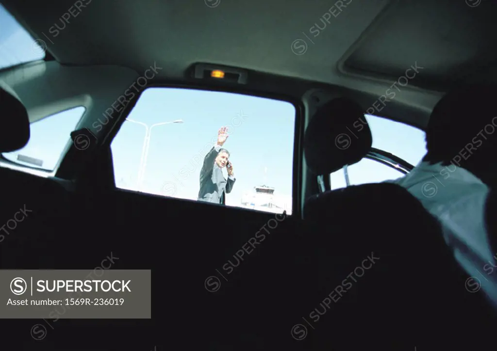 Businessman seen through taxi car window waving hand, hailing taxi car