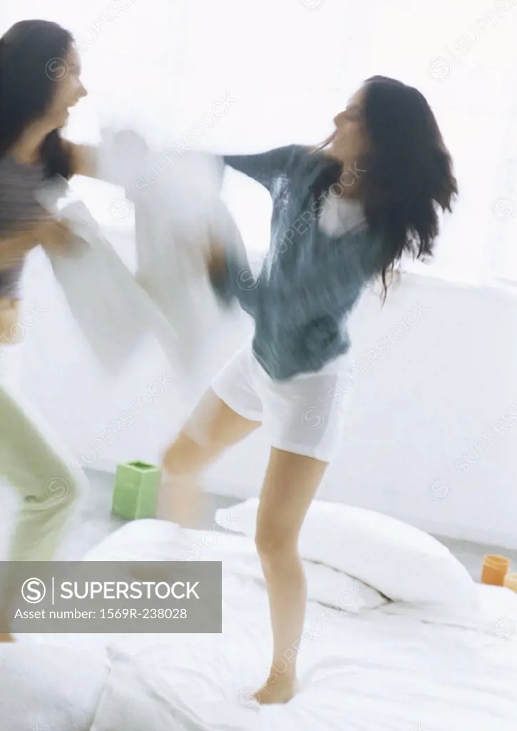 Two young women fighting with pillows, blurred motion