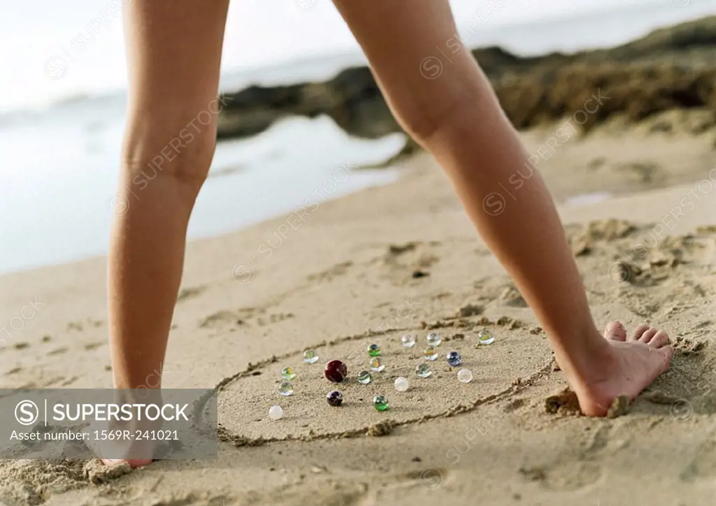 Child´s legs above marbles on sand, low section, close-up