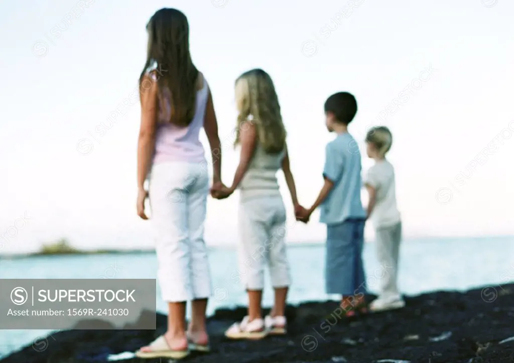 Children standing, holding hands, looking out to sea