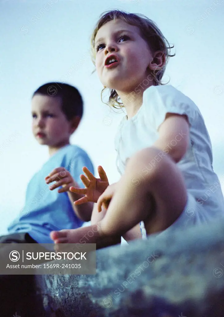Two children sitting outdoors, low angle view