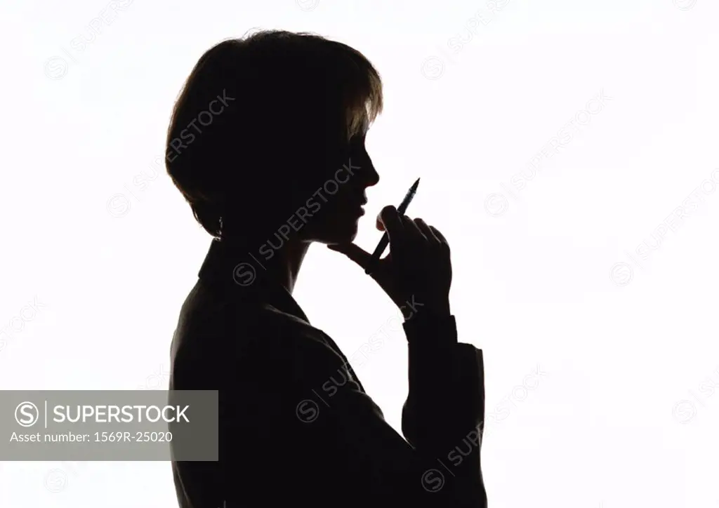 Woman holding pen near mouth, silhouette