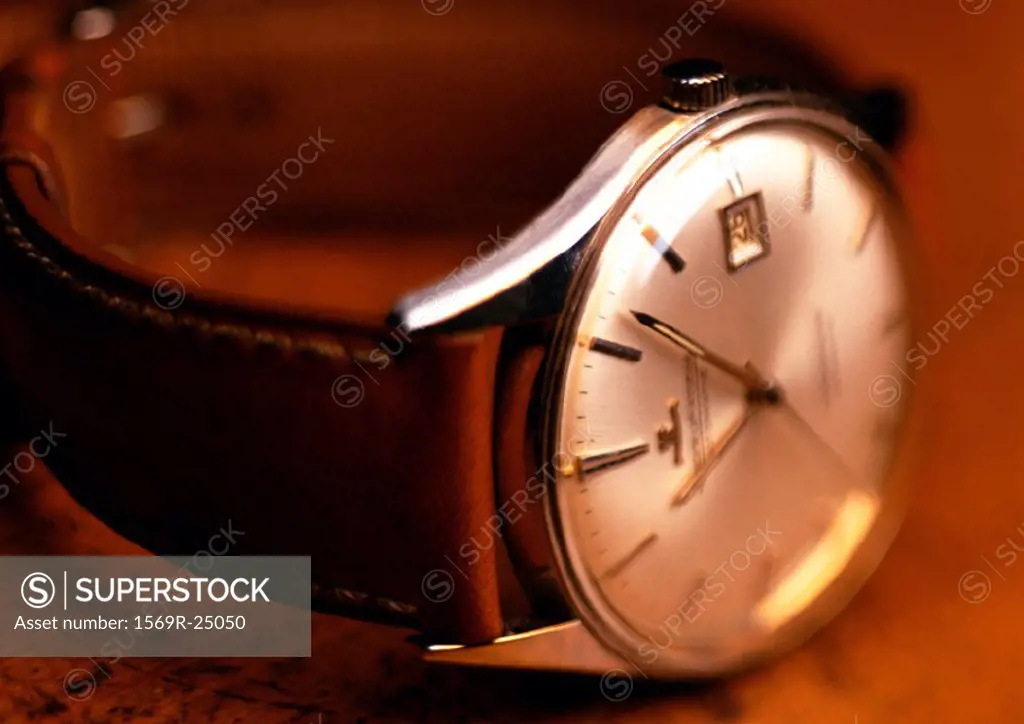 Wristwatch with white face and leather band, wood background, close-up