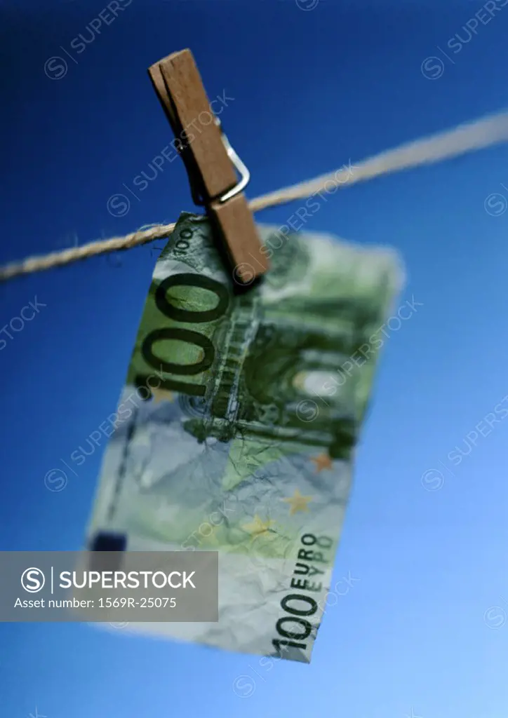 Wrinkled hundred euro bill hanging on clothesline with clothes peg
