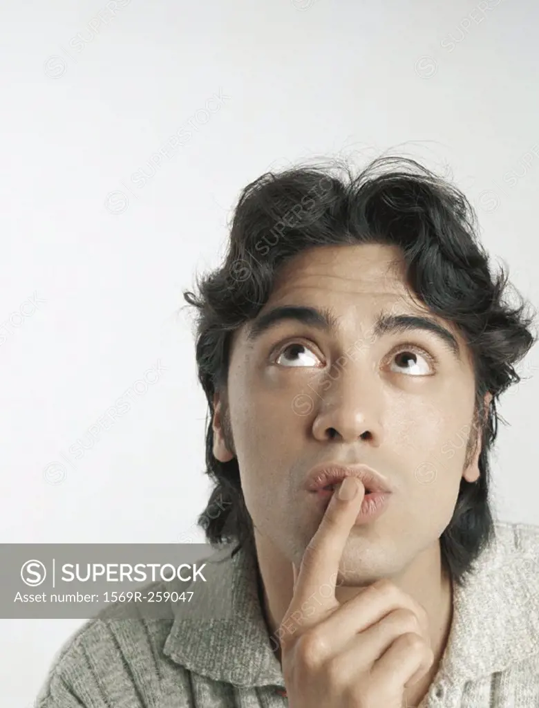 Young man looking up with finger on lips