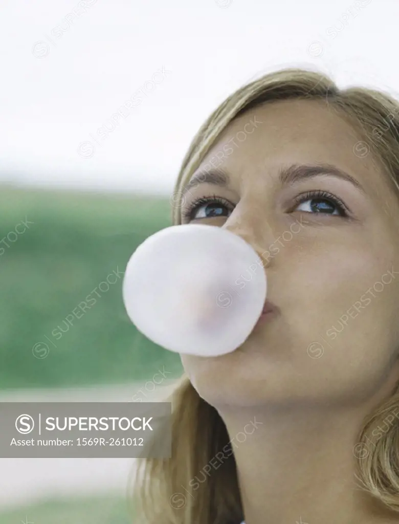 Young woman blowing bubble with chewing gum, looking up, close-up