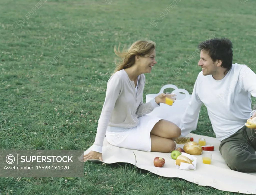 Young man and young woman sitting on blanket on grass having picnic