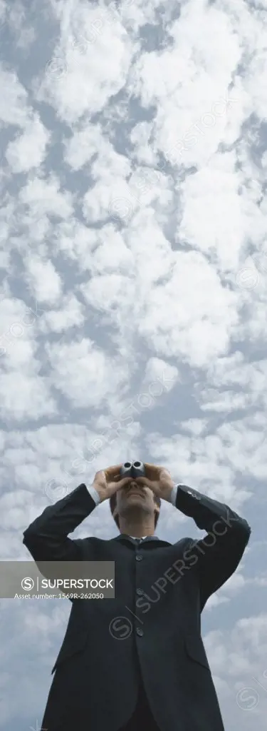 Man looking through binoculars, sky in background, low angle view