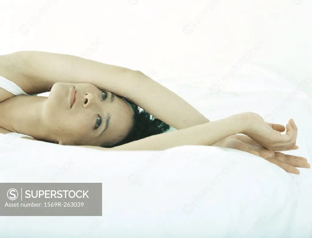 Woman lying on bed with arms crossed at wrists above head