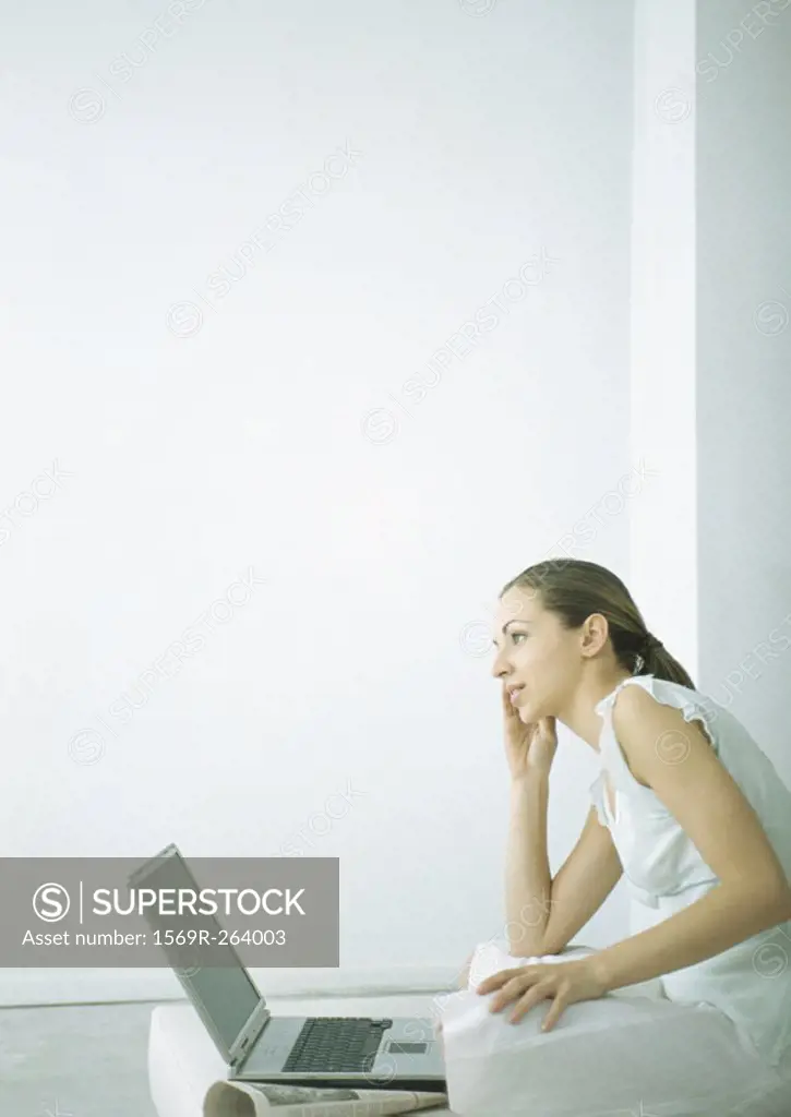 Young woman sitting on floor with laptop, holding cell phone to ear