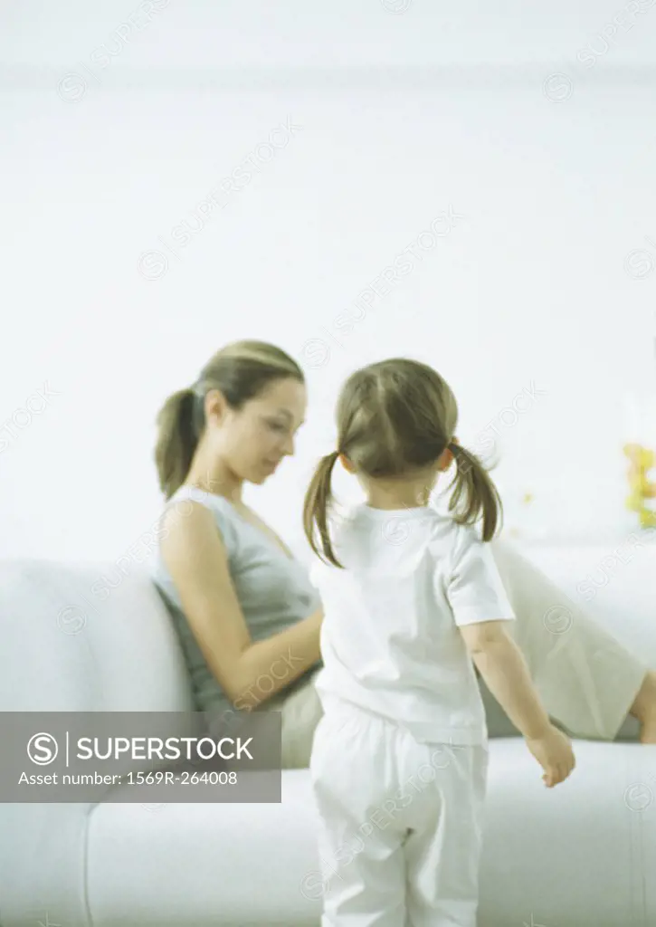 Little girl with pigtails, rear view, and young woman sitting on sofa
