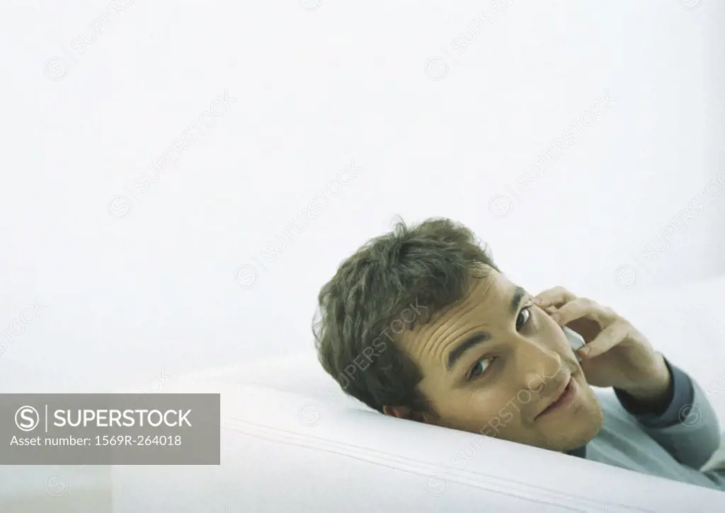 Man sitting on sofa, looking back over shoulder, holding cell phone to ear