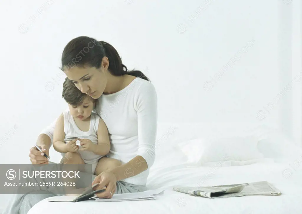 Woman sitting on edge of bed with little girl on lap, looking down at agenda