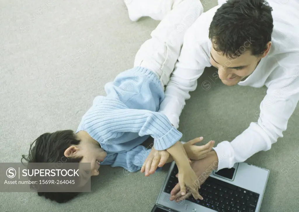 Man and little boy lying on floor with laptop playing