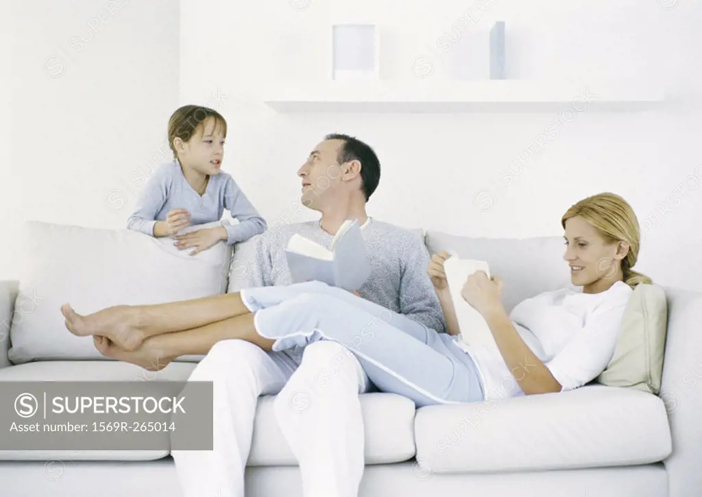 Parents sitting on sofa, girl standing behind sofa talking to father
