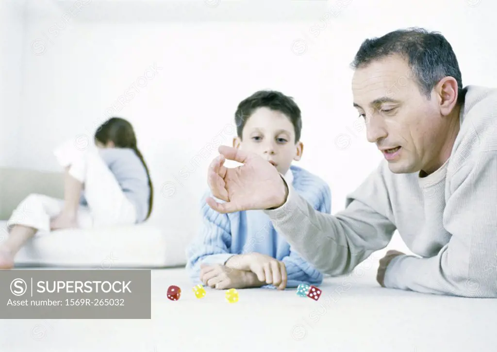 Man and son playing dice on floor, girl sitting in background