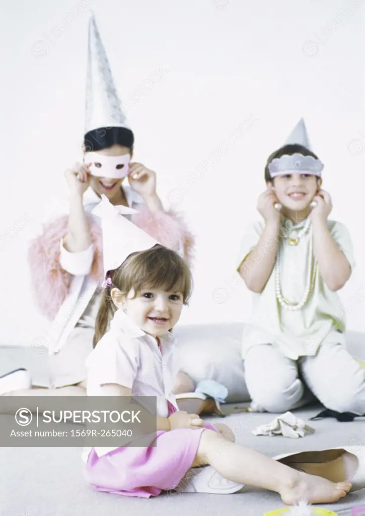 Mother sitting on floor with boy and girl, wearing party hats and disguises