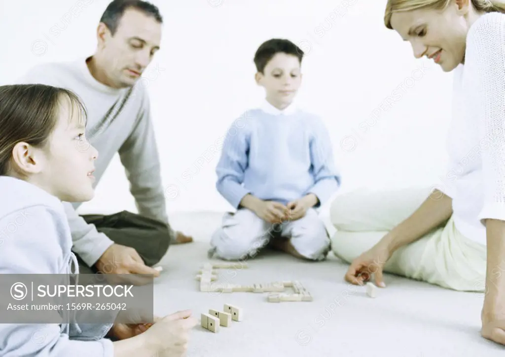 Girl and boy with parents playing dominoes on floor