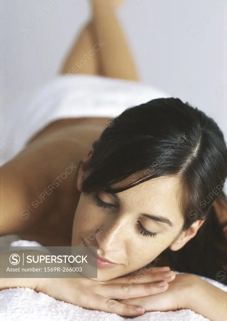 Woman lying on stomach with eyes closed and hands under chin