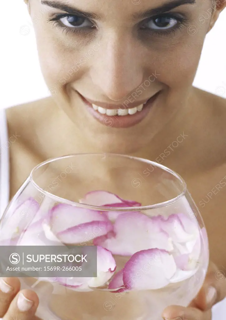 Woman holding bowl of water and rose petals, looking at camera, close-up