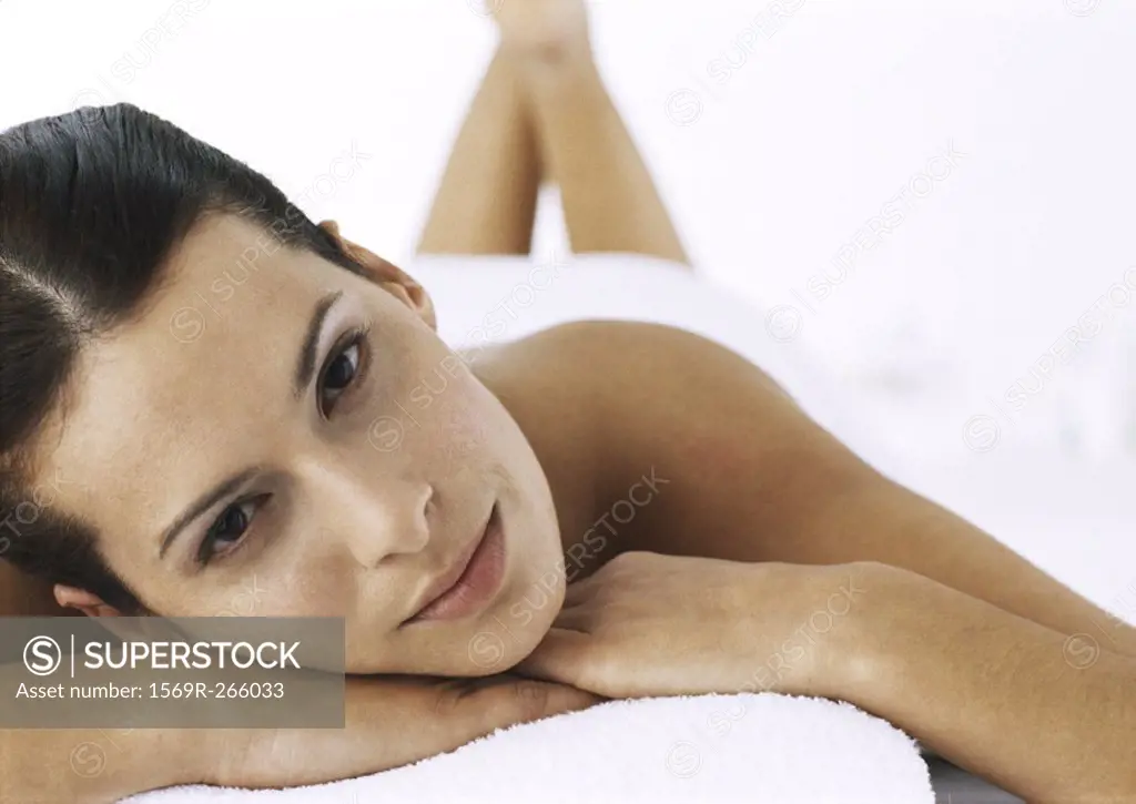 Woman looking at camera, lying on massage table with legs up, focus on face in foreground