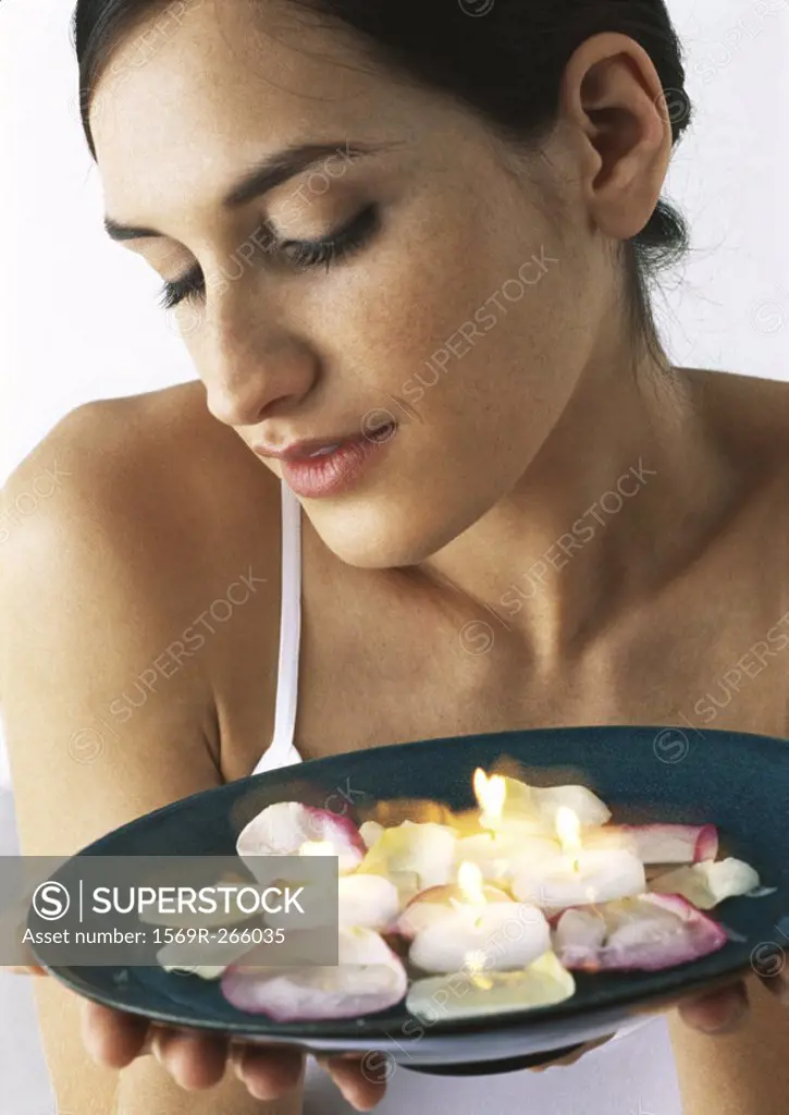 Woman holding plate of candles and rose petals, looking down, close-up