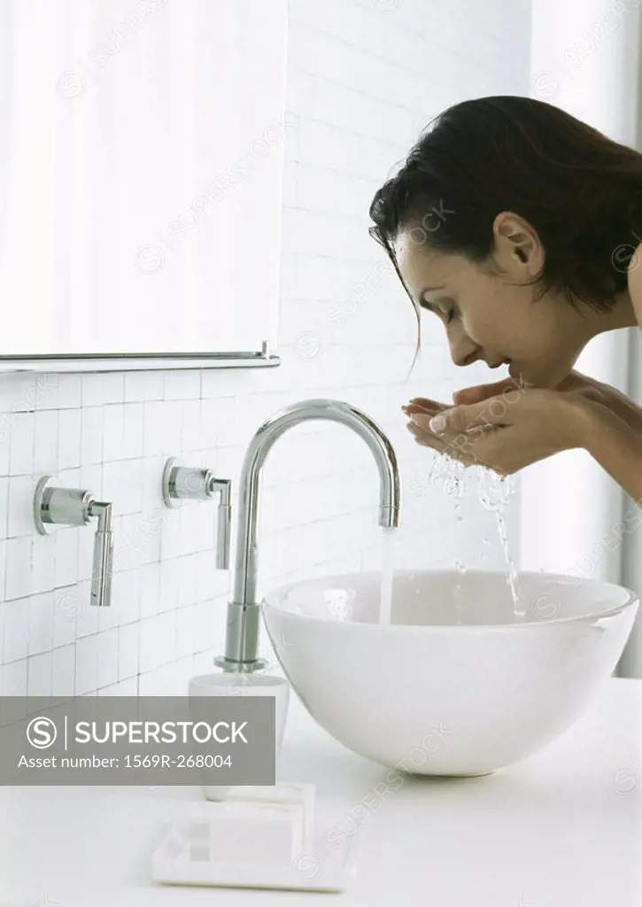 Woman bending over sink cupping water in hands beneath face