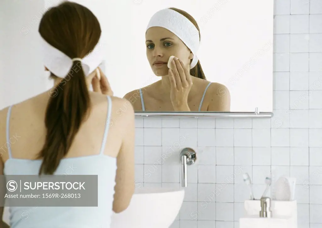 Woman washing face in front of mirror