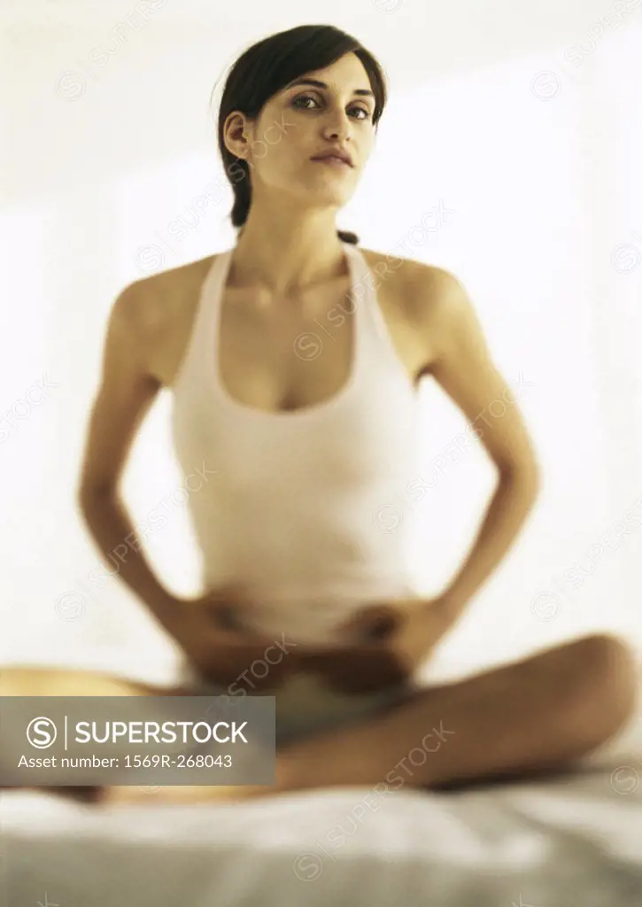 Woman sitting indian style touching stomach on bed