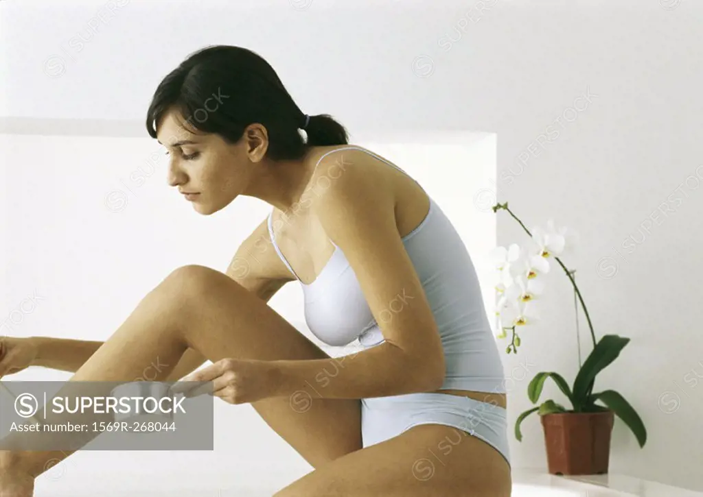 Woman sitting in underclothes applying hot wax to leg