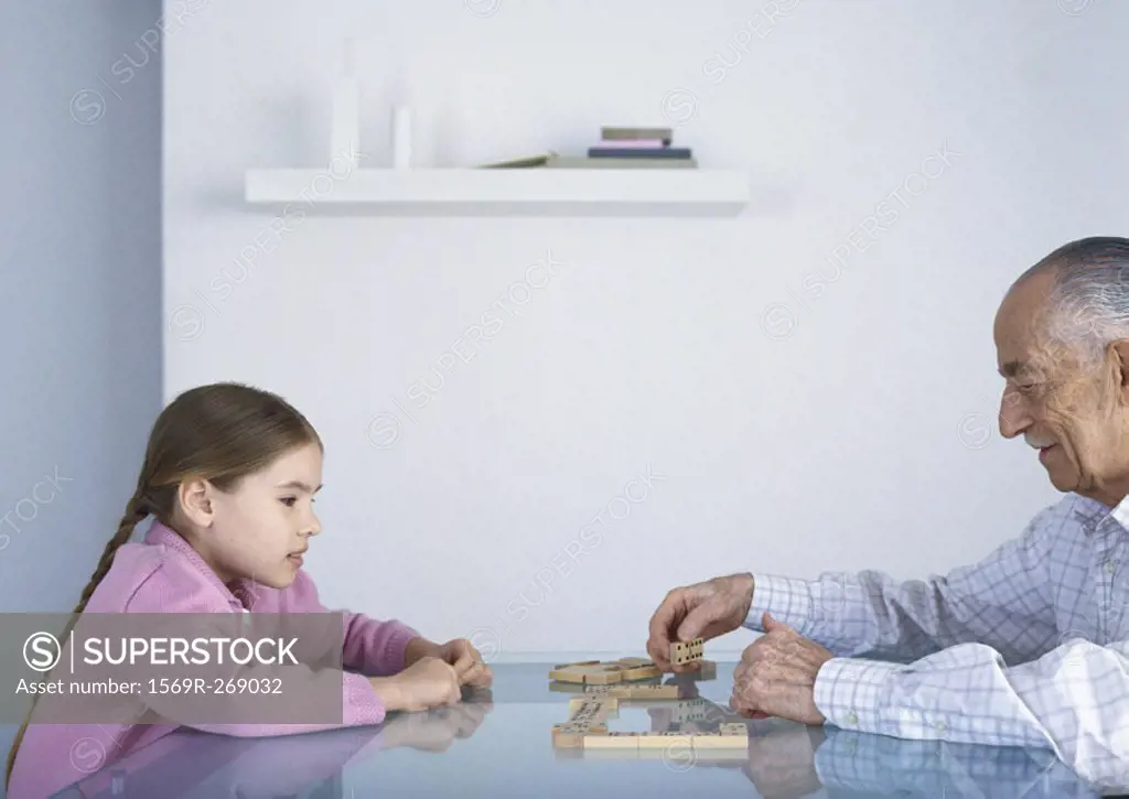 Grandfather and girl sitting at table playing dominoes