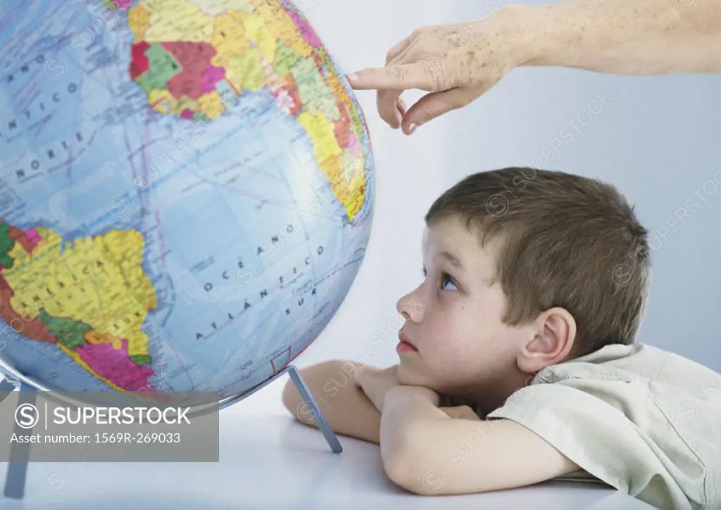 Boy looking at globe, elderly person´s hand pointing to spot on globe