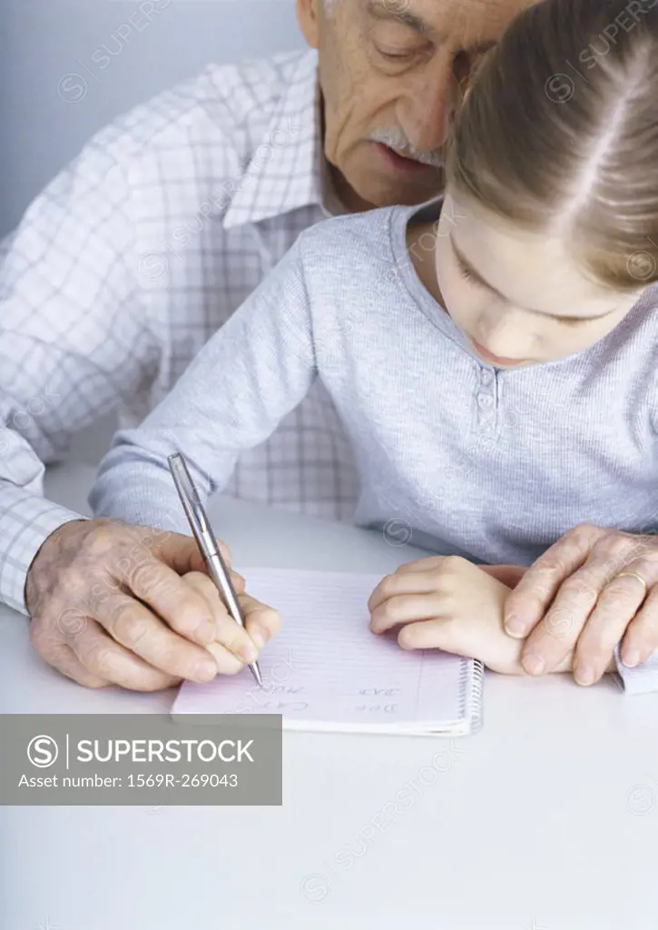 Grandfather helping girl write in notebook