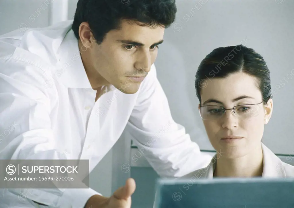Woman working at computer, man leaning over shoulder gesturing to screen