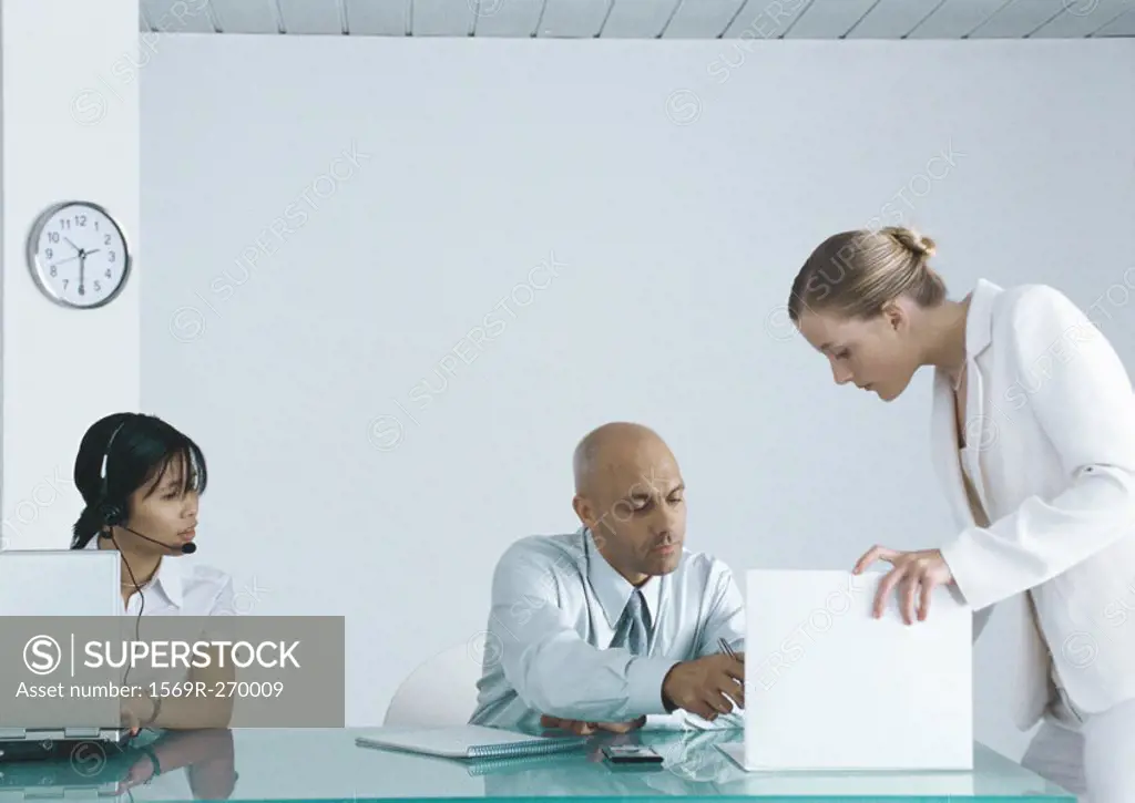 Woman at computer with headset sitting next to businessman signing document held by second woman