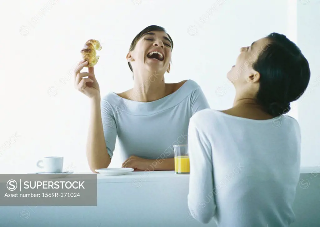 Two women on either side of bar having breakfast, laughing