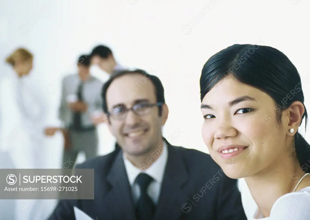 Businesspeople smiling at camera, in background businesspeople taking coffee break