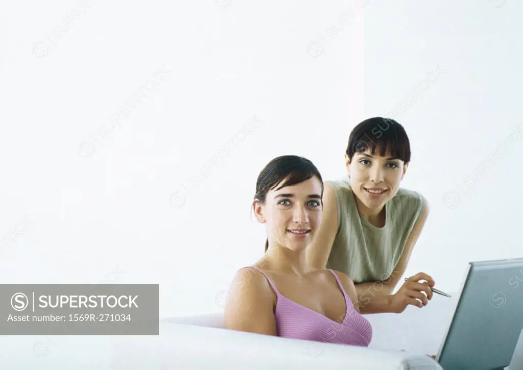 Woman sitting on sofa with laptop, second woman behind leaning on sofa