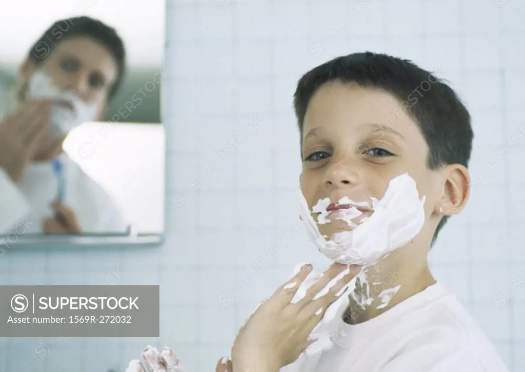 Boy with shaving cream on face and hands, man shaving in background