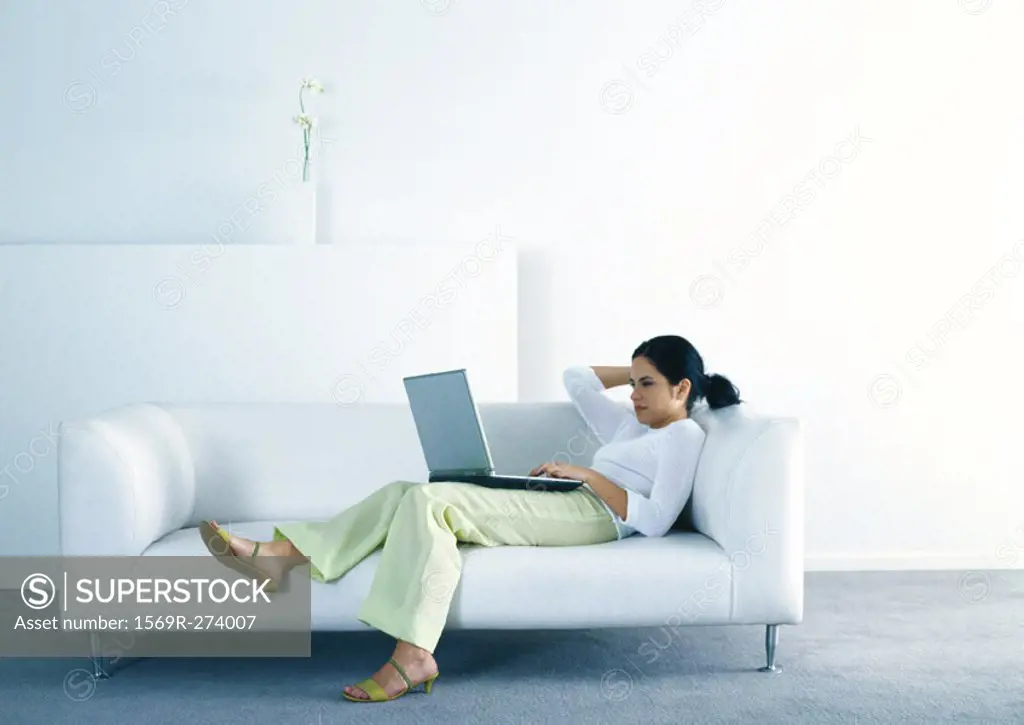 Woman lounging on sofa and using laptop
