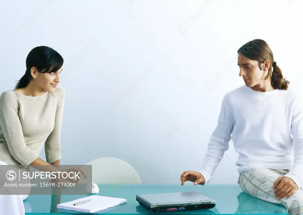 Man and woman sitting on table, woman flicking paper ball to man