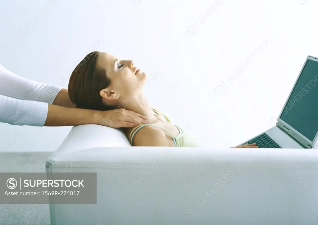 Woman sitting on sofa with laptop, having neck massaged