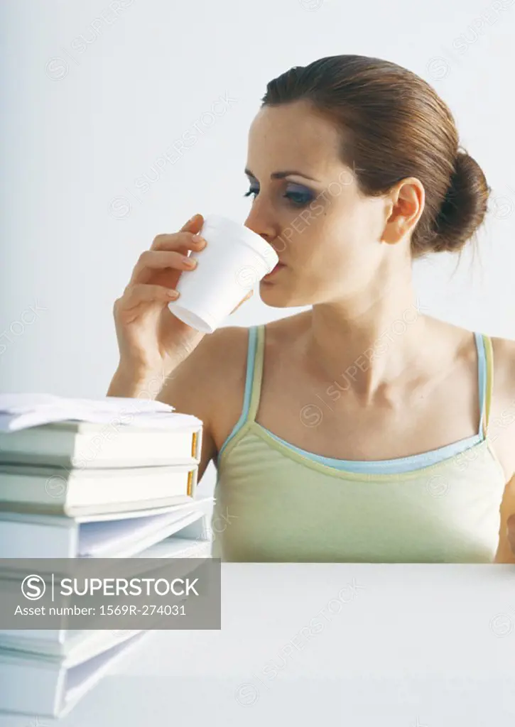 Woman drinking at table with stack of folders