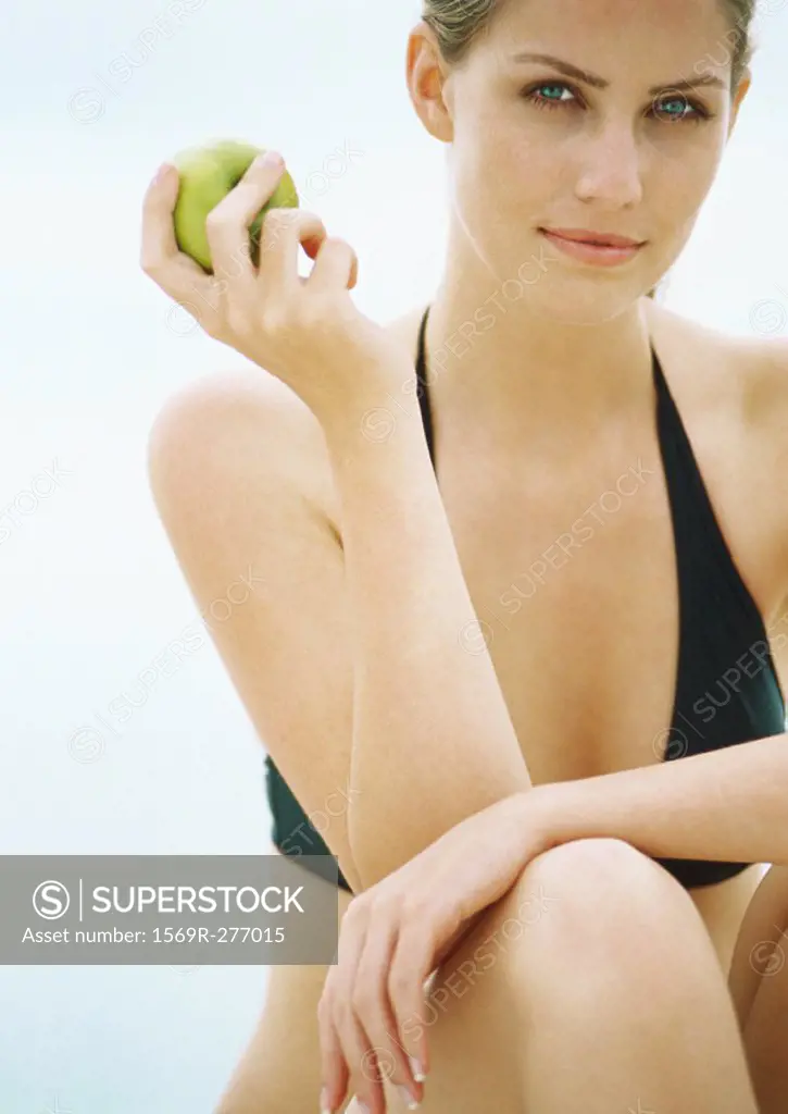Young woman in bikini holding apple, looking at camera